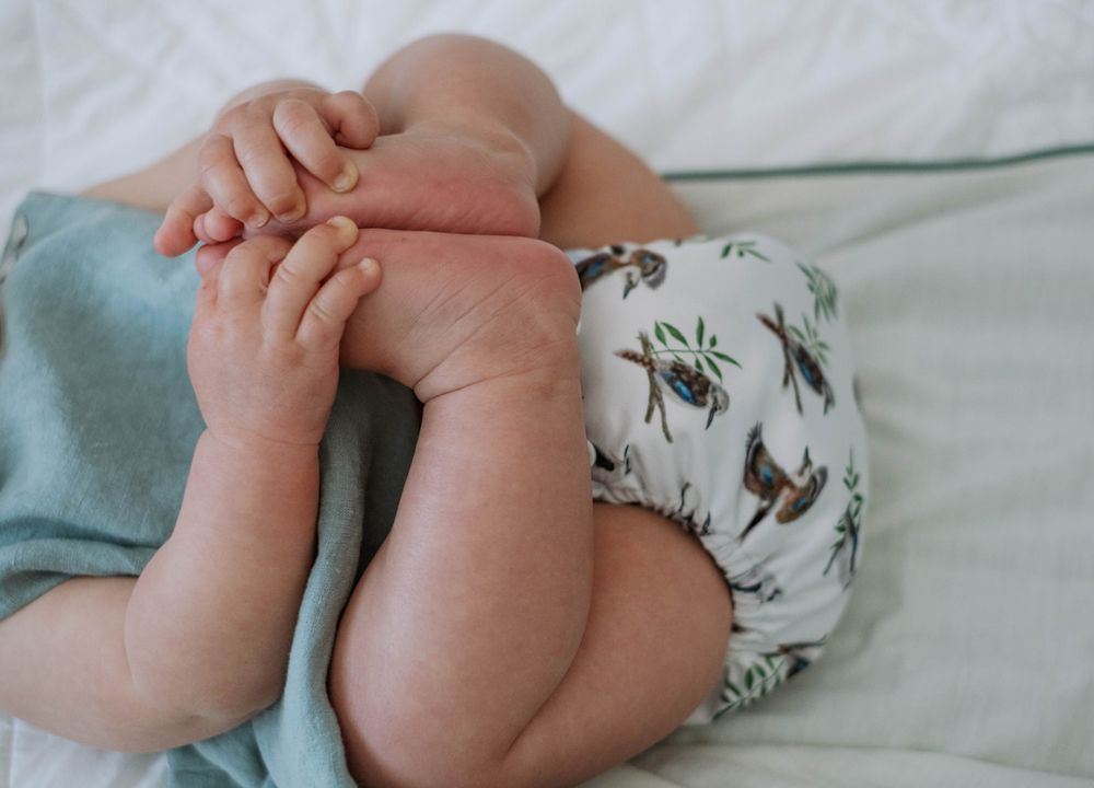 Baby holding feet wearing a Kookaburra cloth nappy 