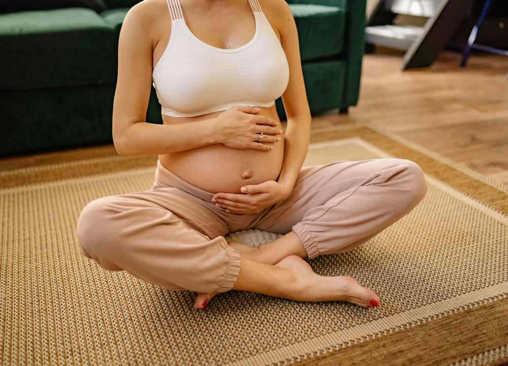 Pregnant woman sat on the floor cross legged holding bump doing breathing exercises