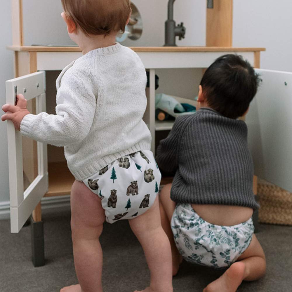 Baby and toddler playing in wooden toy kitchen both wearing reusable nappies