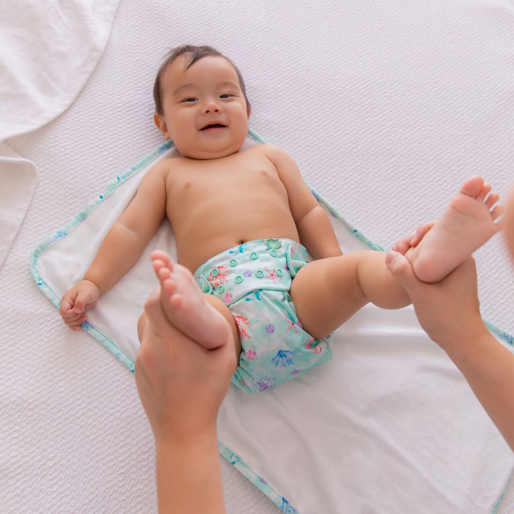 Cute Asain baby smiling wearing reusable nappy with mother holding his feet up playfully