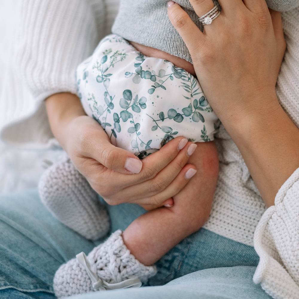 Close up of mother's hands holding newborn baby. Baby is wearing eucalyptus reusable nappy