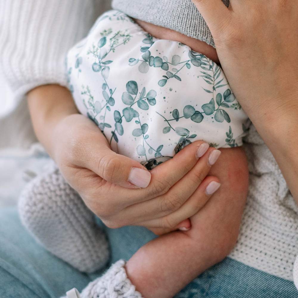 Mother holding her newborn baby, image is close up showing mother's hands and baby's eucalyptus print reusable nappy