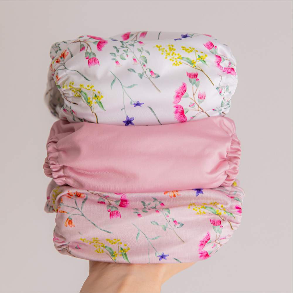Hand holding stack of reusable diapers: pink australiana, pink lemonade, and australian florals