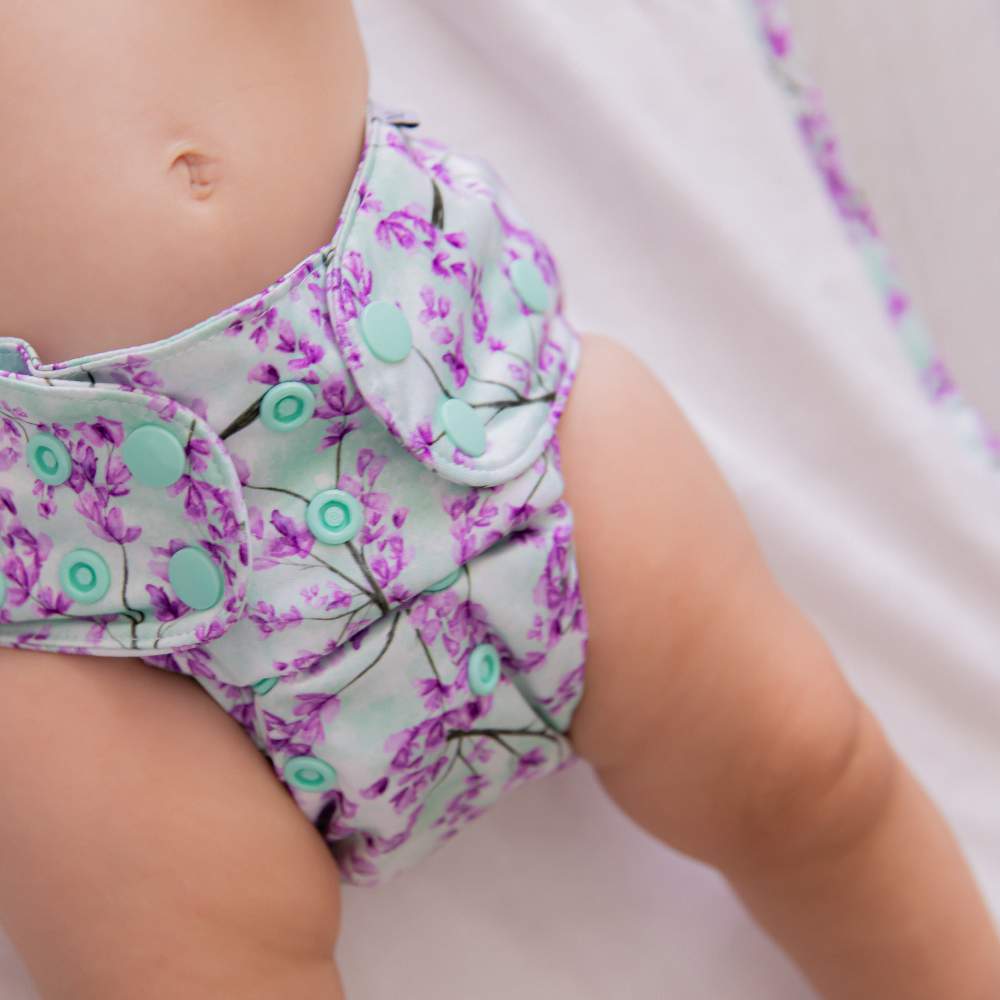 Close up of baby tummy and thighs laying on change mat wearing jacaranda bloom reusable nappy