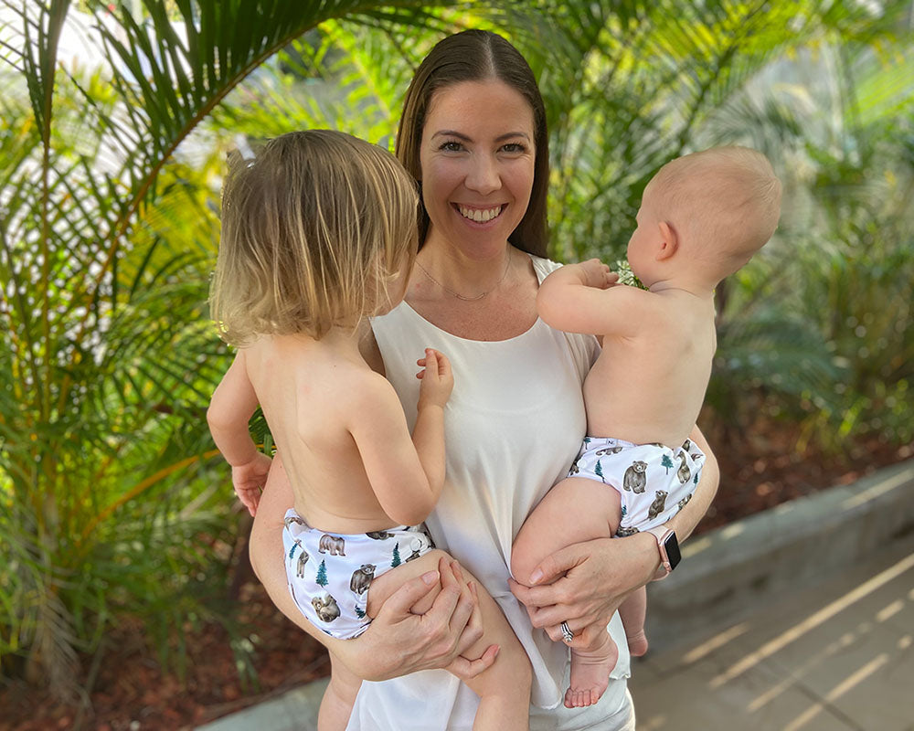 Jen holding her children who are wearing bear cub reusable cloth nappies with palm trees behind