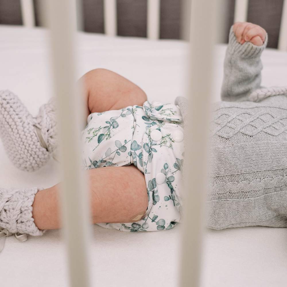 Image through cot bars shows newborn baby in cot wearing eucalyptus cloth nappy