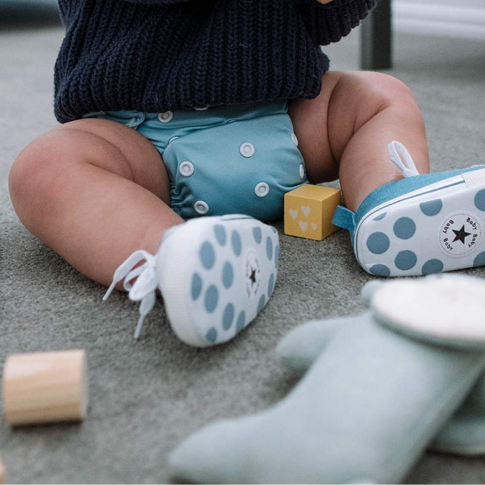 Baby sat on the floor playing with wooden toys wearing blue sea breeze reusable nappy