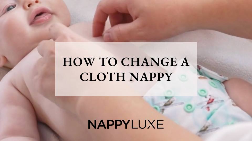 Image of young baby laying on change mat being tickled by mother's hands. Baby is wearing aeroplane cloth nappy.