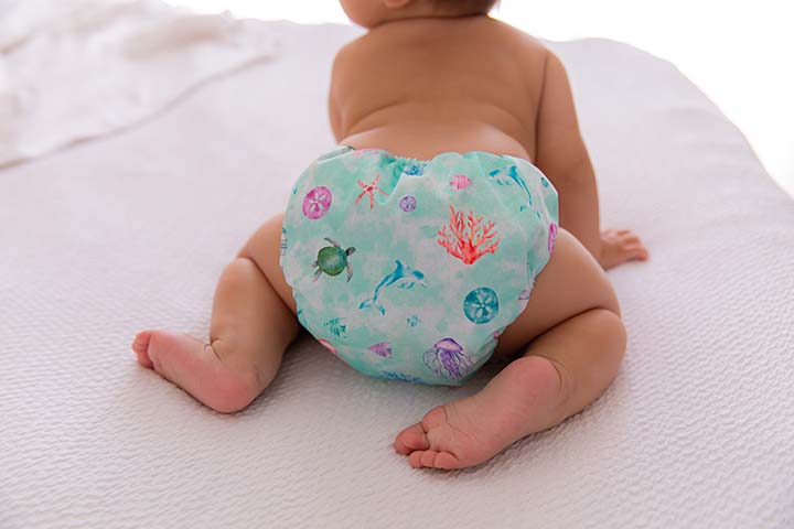Baby on all fours on white bed in ocean themed cloth nappy