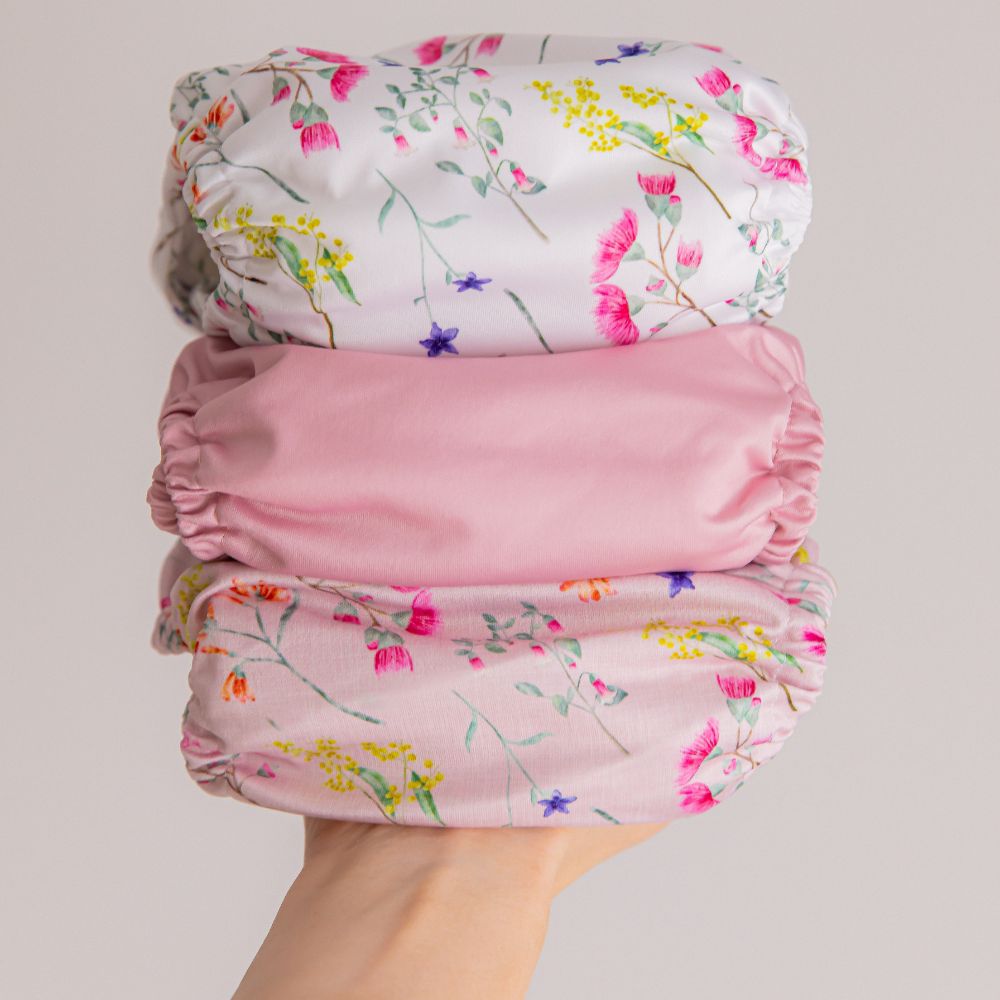 A hand holding up a stack of 3 floral and pink cloth nappy prints.
